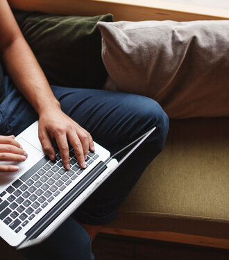 Mensch arbeitet mit dem Laptop auf dem Sofa.