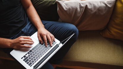 Mensch arbeitet mit dem Laptop auf dem Sofa.